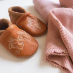 Dettaglio del kit regalo nascita rosa sorbetto con copertina, doudou in maglia e scarpine con ricamo anatra